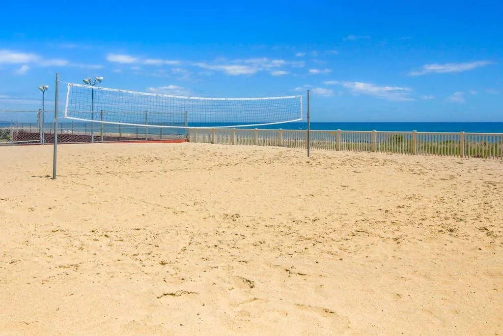A sandy beach volleyball court with a net beside the ocean.