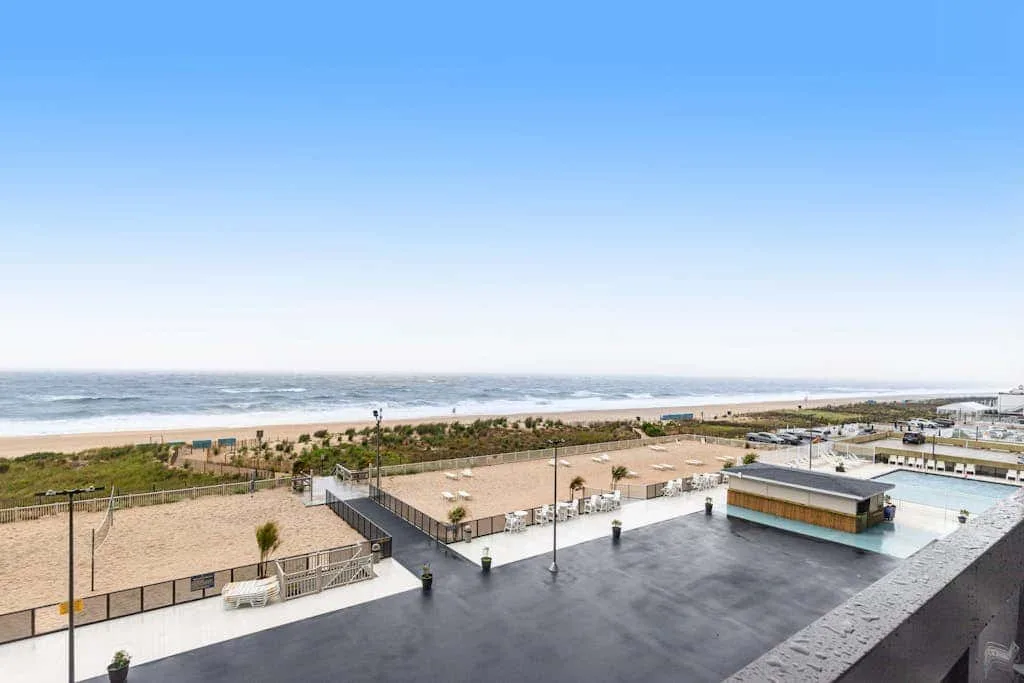 A rooftop terrace overlooks the beach and ocean under a clear sky.