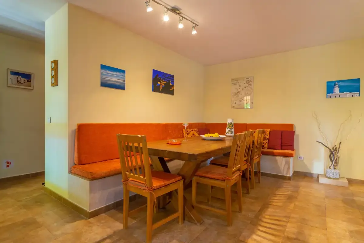 Un comedor con una mesa de madera y sillas junto a un banco tapizado de color naranja.