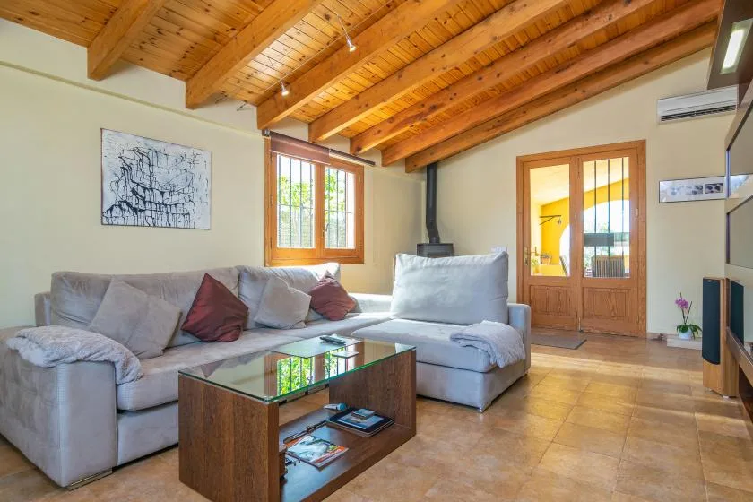 Una sala de estar con asientos grises, una mesa de centro de cristal y techo de madera.