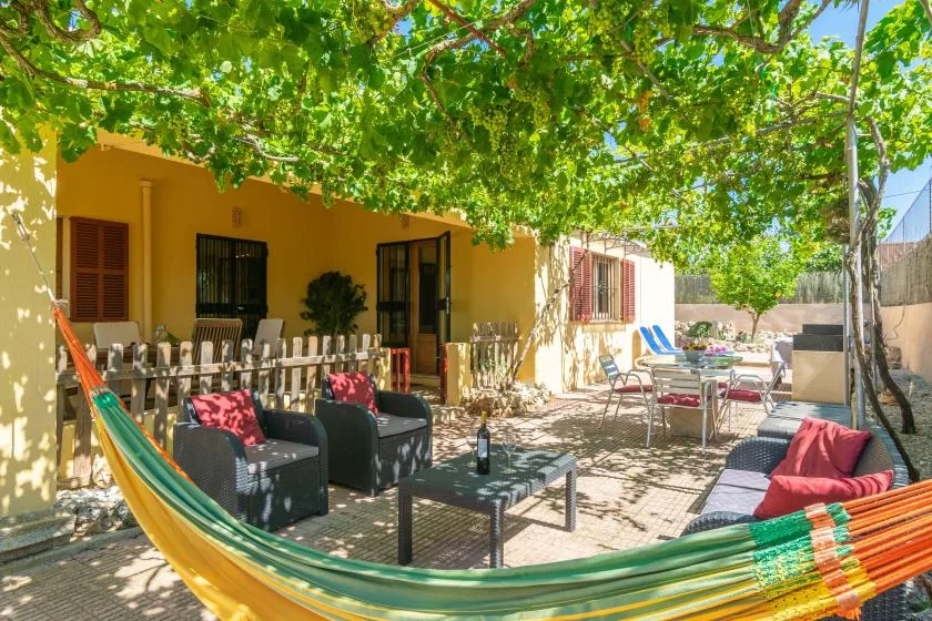 Un patio exterior sombreado con asientos bajo una frondosa parra.