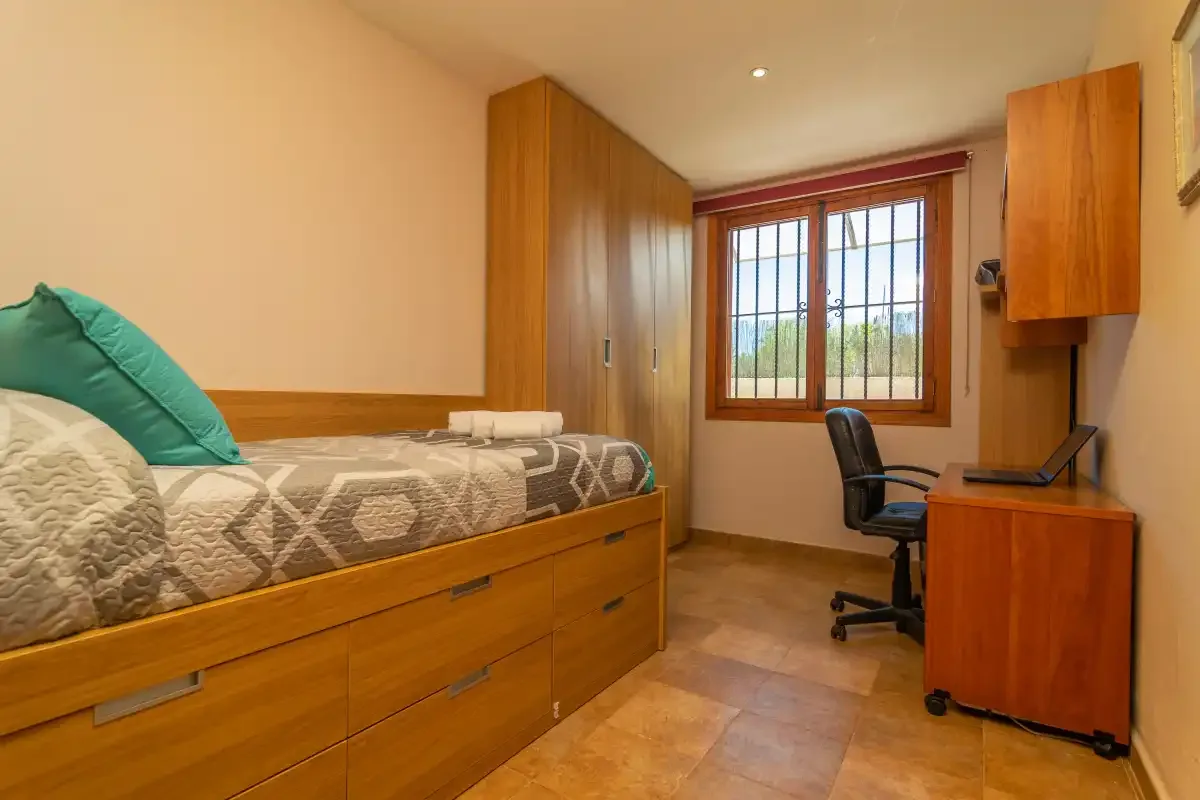Un dormitorio con cama de madera, armarios y un escritorio junto a la ventana.