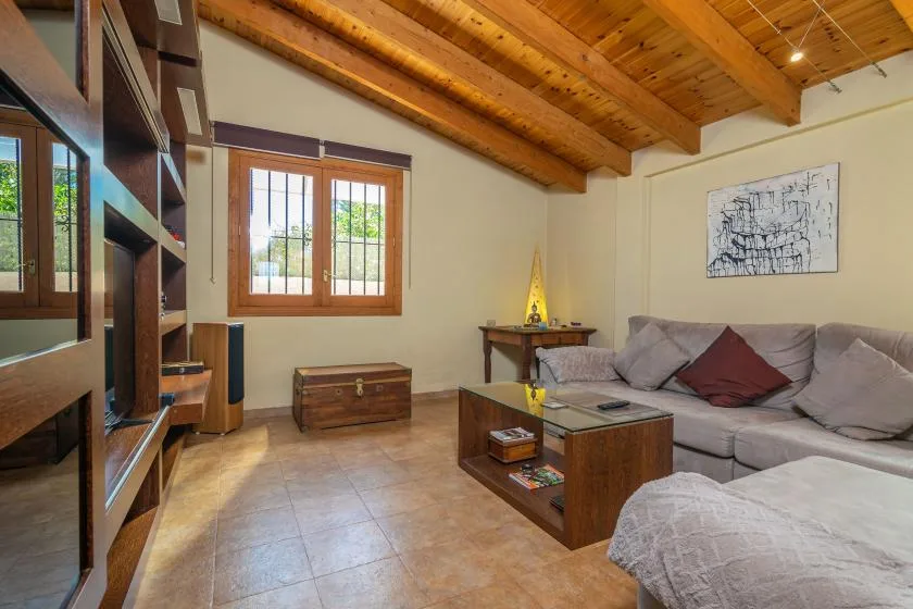 Una sala de estar con sofá seccional, mesa de centro y vigas de madera expuestas en el techo.