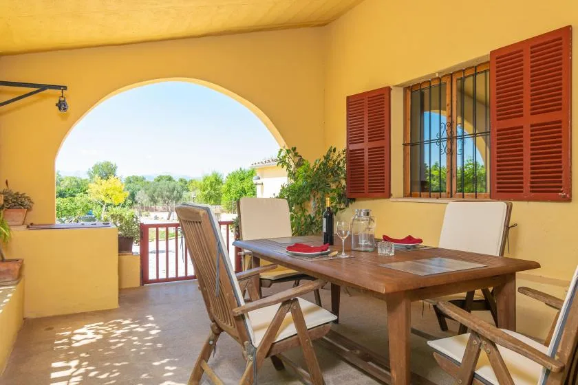 Comedor exterior cubierto con una mesa de madera y sillas junto a un arco abierto.