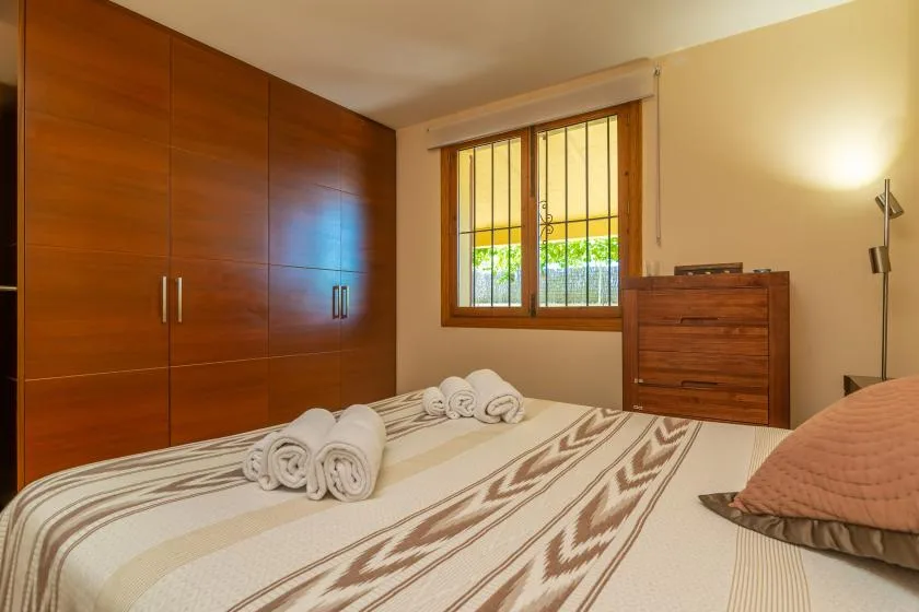 Un dormitorio con una colcha estampada, armarios de madera y una ventana.