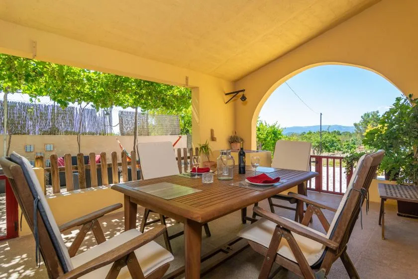Comedor exterior cubierto con una mesa de madera y vistas a la vegetación.