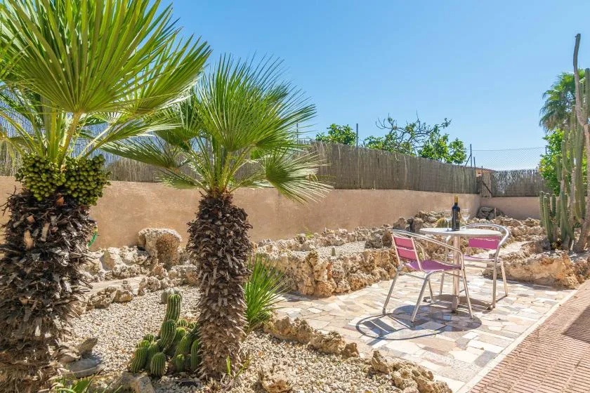 Un patio soleado de piedra con una mesa metálica, sillas y palmeras.