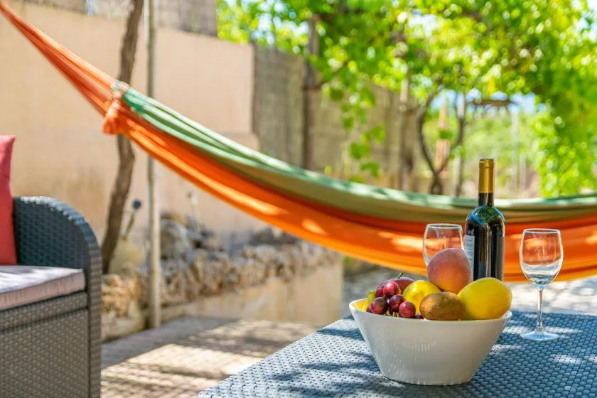 Una zona de comedor exterior a la sombra, con una hamaca y una mesa con fruta y vino.