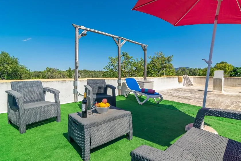 Una terraza en la azotea con asientos al aire libre, una tumbona y una sombrilla roja.