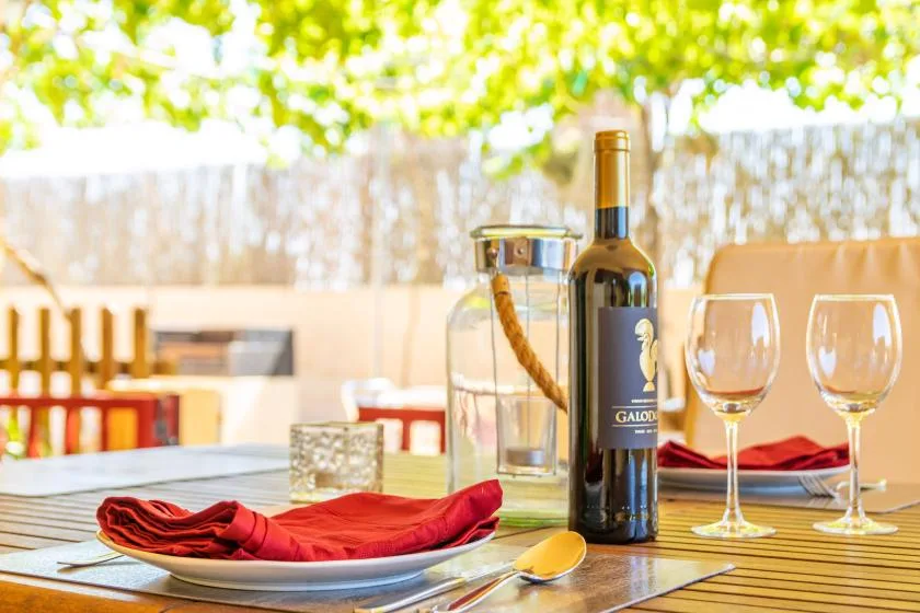 Una mesa de comedor al aire libre con servilletas rojas y una botella de vino.