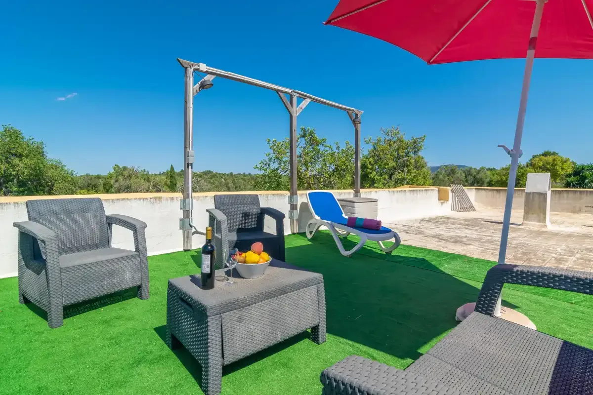 Una terraza en la azotea con asientos de mimbre, una tumbona y una sombrilla roja.