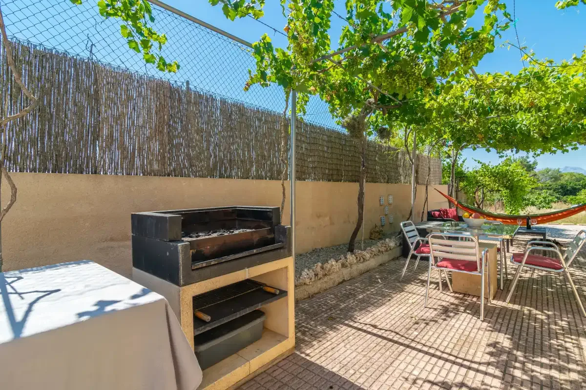 Una zona de comedor al aire libre con una parrilla y sombra de hojas.