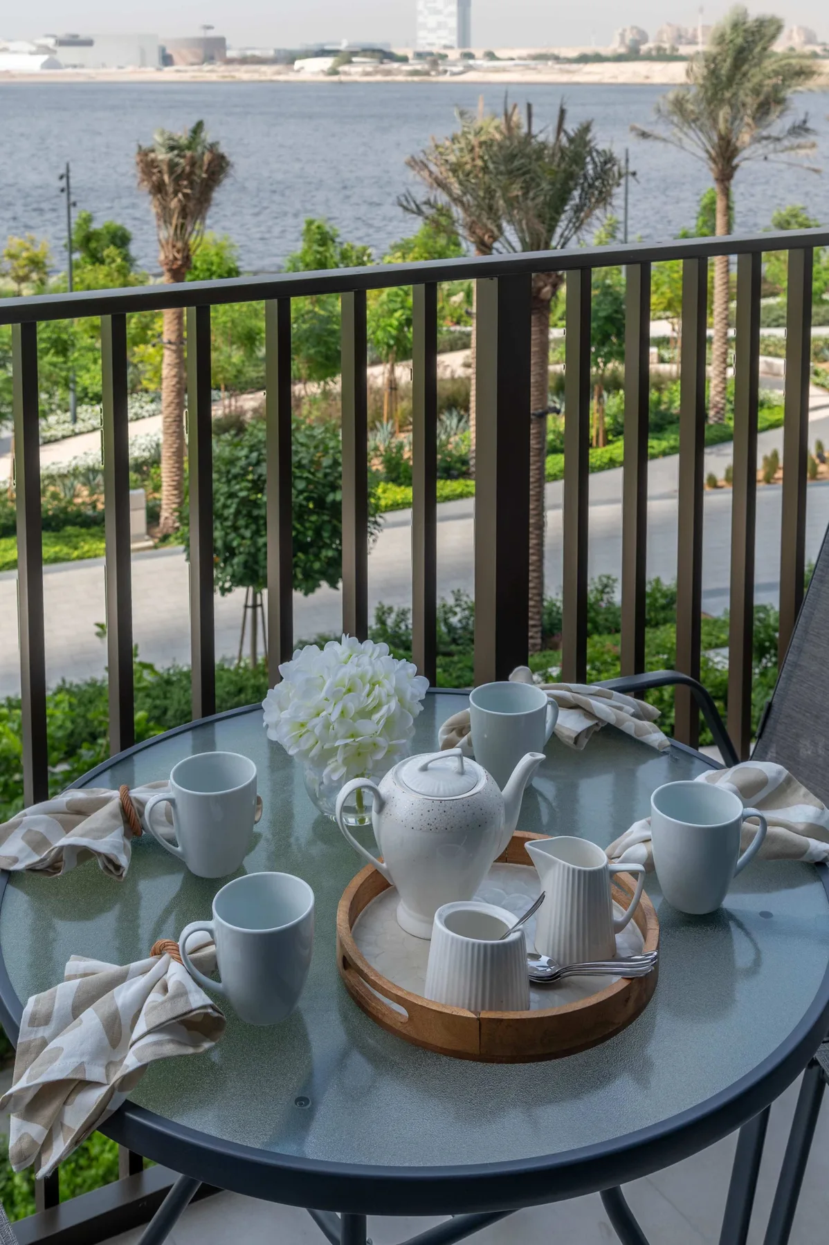 Una mesa de balcón está preparada con té y flores, con vistas al agua.