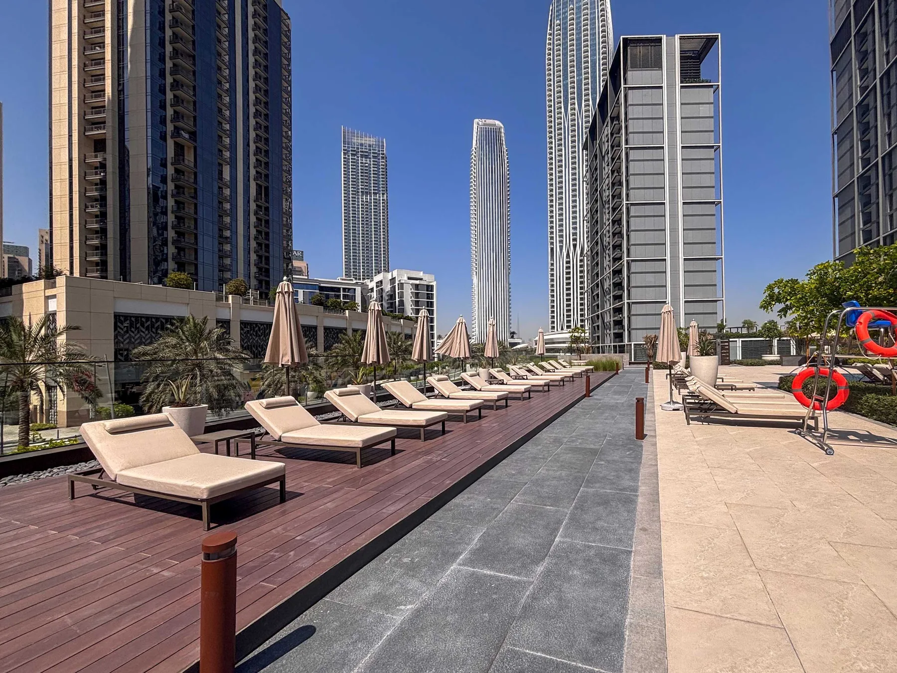 Una terraza de piscina en la azotea con tumbonas y edificios altos al fondo.