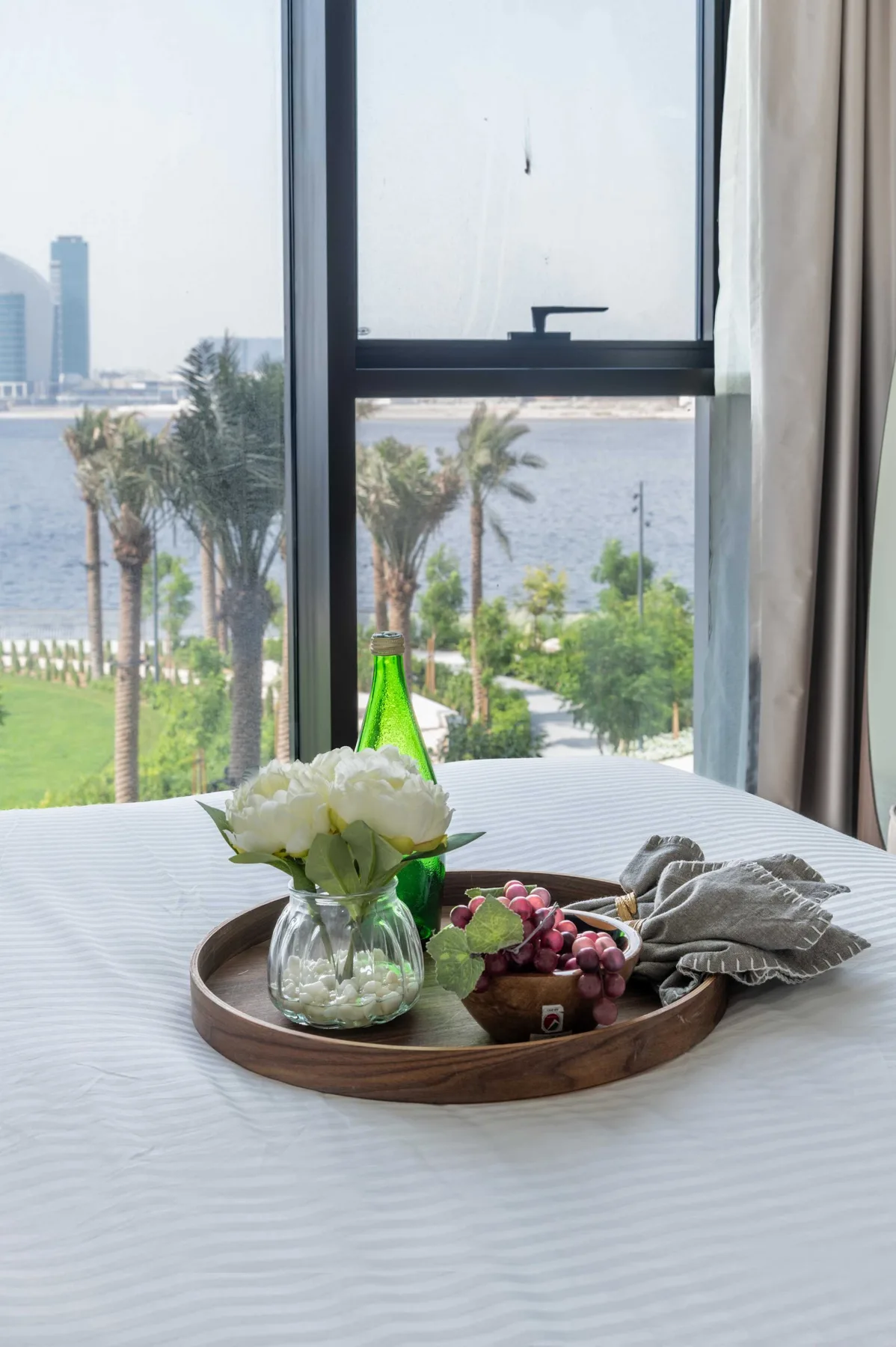 Un dormitorio con una bandeja de flores y fruta junto a una ventana con vistas al agua.