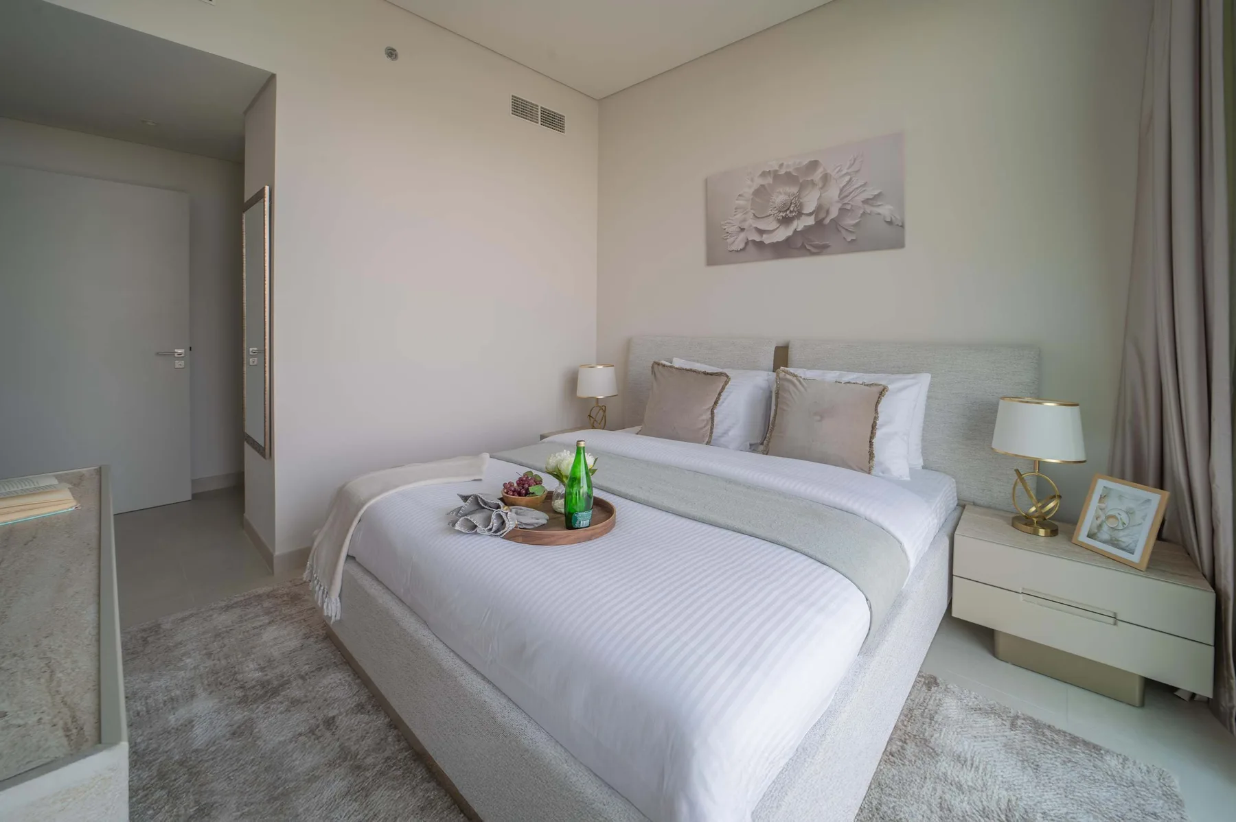 Un dormitorio luminoso con una cama bien tendida y arte floral en la pared.