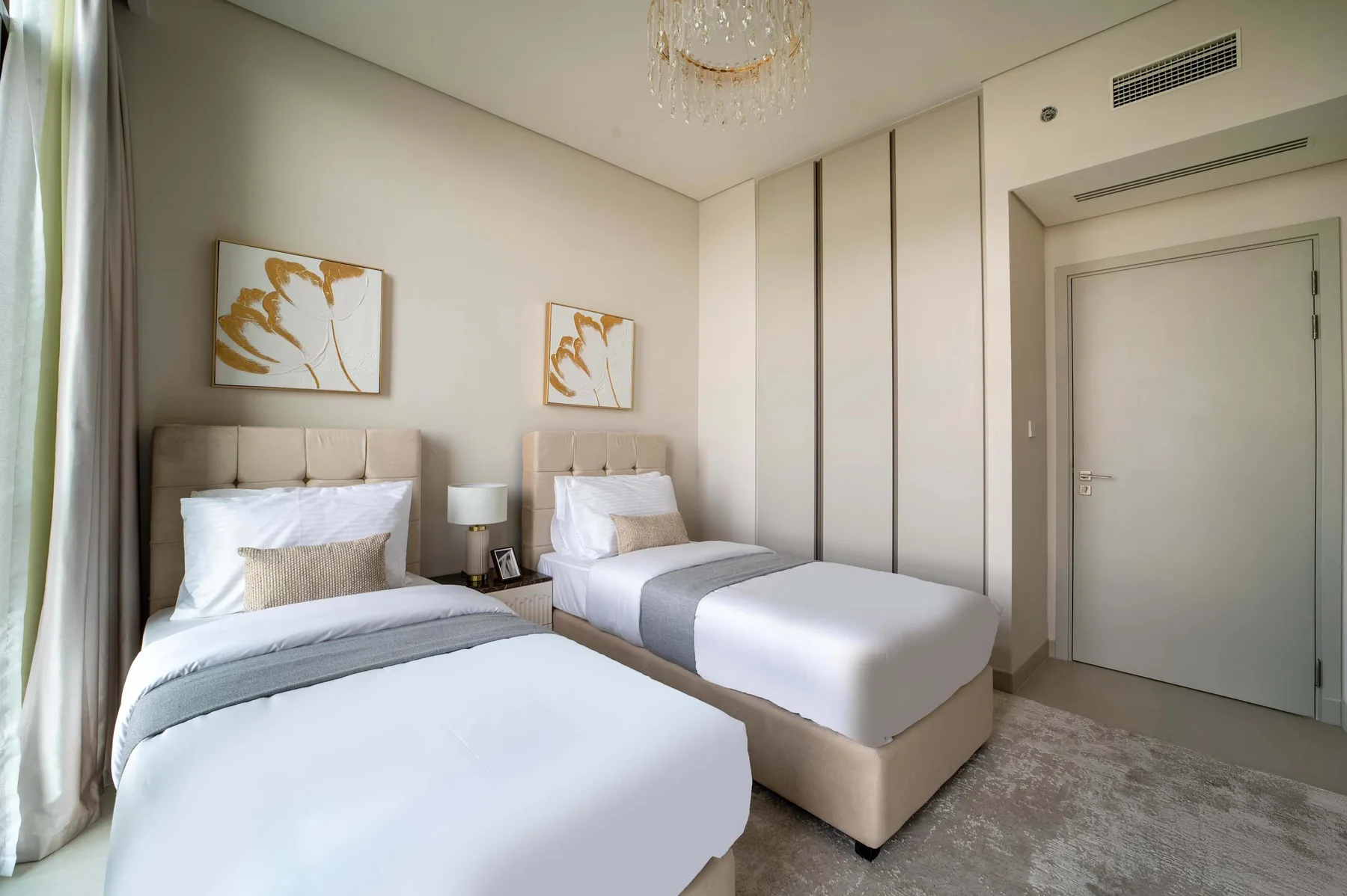 Un dormitorio luminoso con dos camas, ropa de cama clara y cuadros enmarcados.