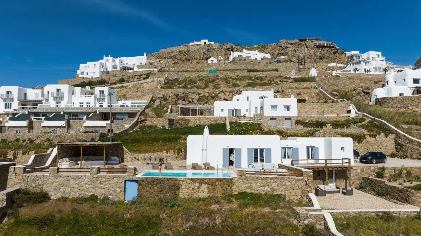 White buildings and terraces dot a rocky hillside beneath a clear blue sky.