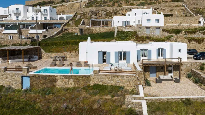 White buildings overlook a swimming pool and stone terraces on a hillside.