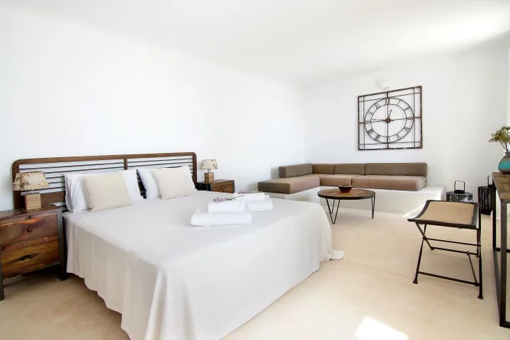 A bright bedroom with a neatly made bed and a sitting area.