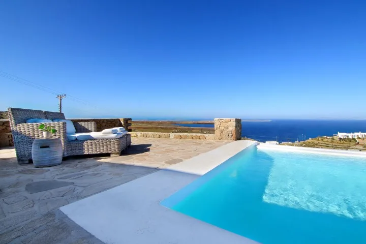 A rooftop pool overlooks the sea, with outdoor seating on the stone terrace.