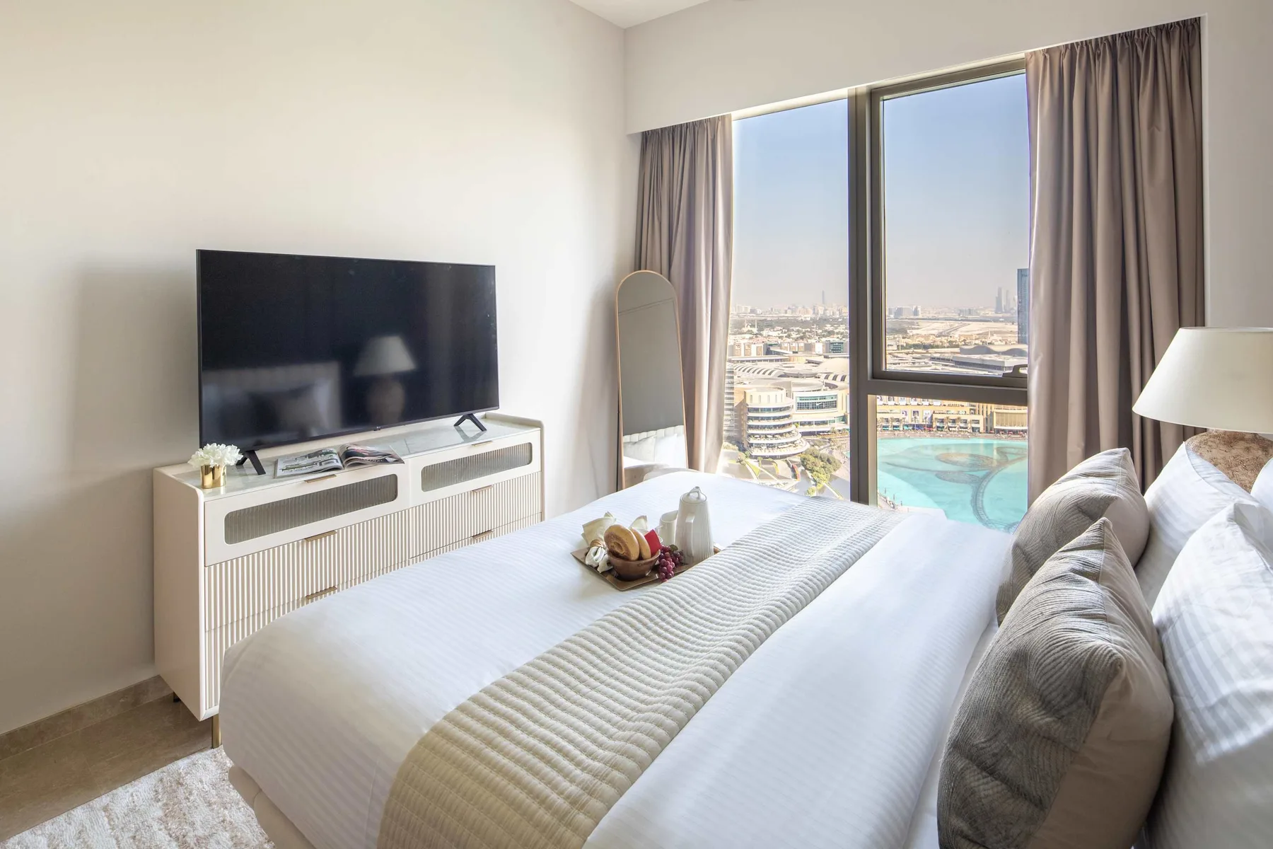 Un dormitorio con cama, televisor y grandes ventanas con vistas a la ciudad.
