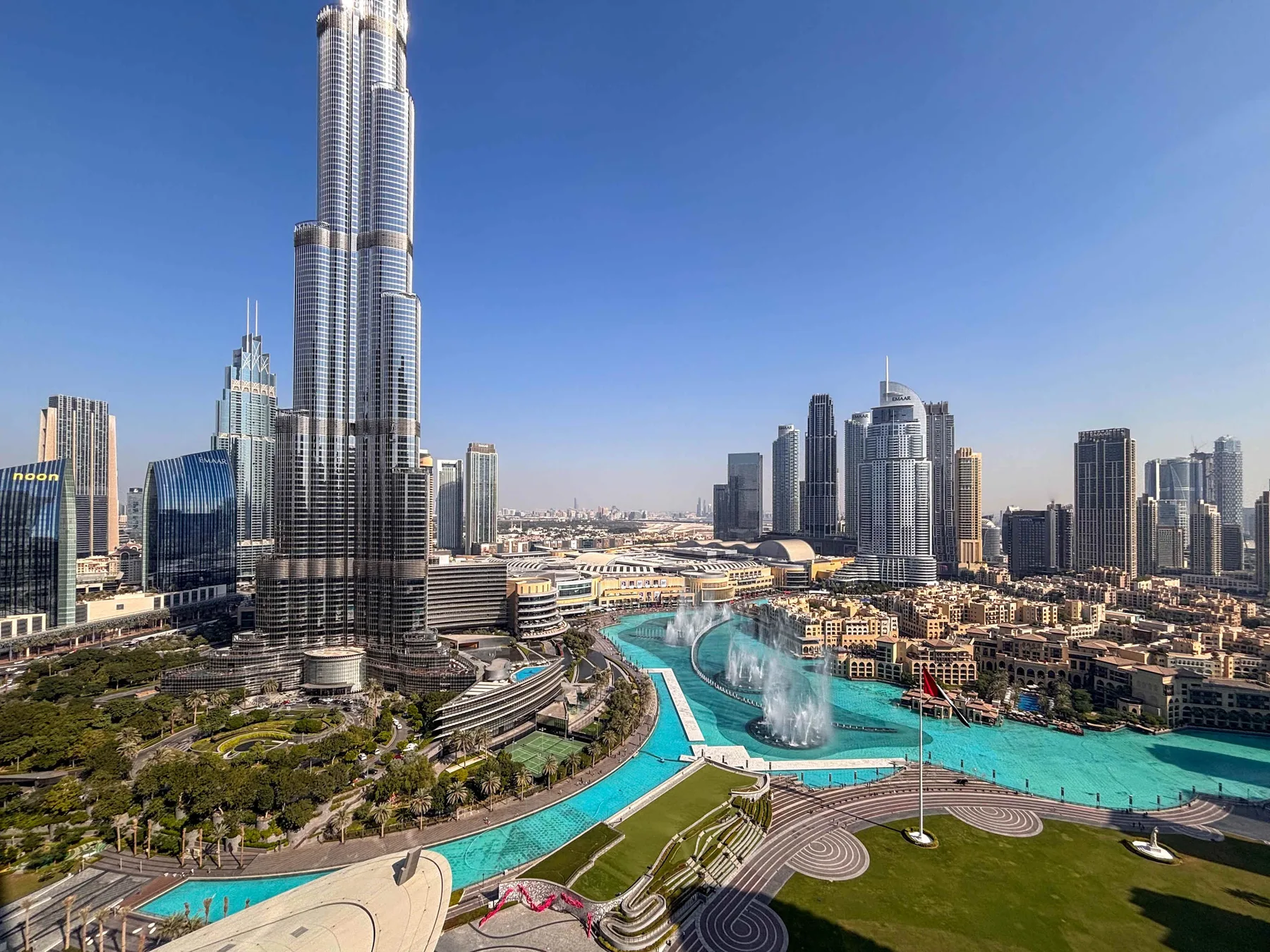 Un horizonte urbano se alza sobre una piscina turquesa con fuentes y jardines.