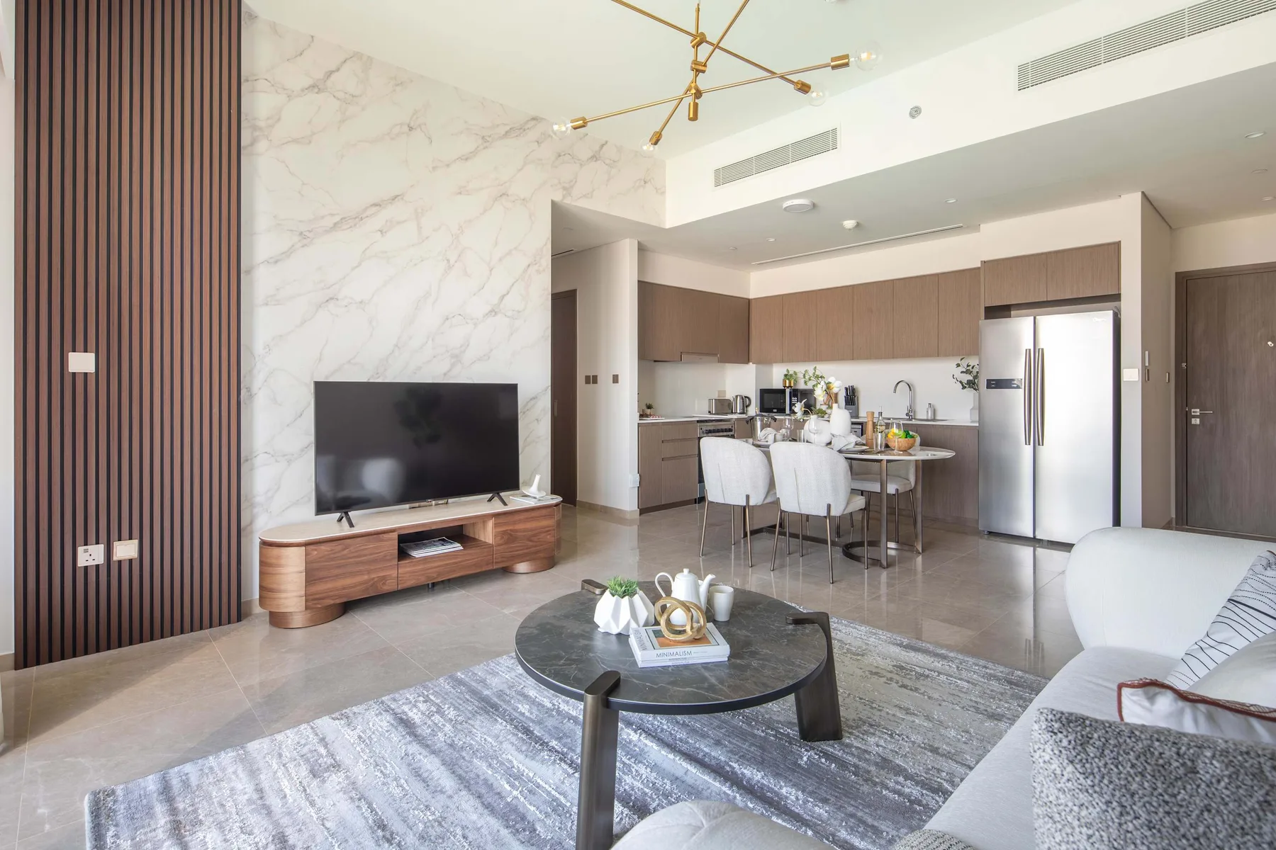 Una sala de estar moderna se abre a una cocina, con televisor y zona de asientos.