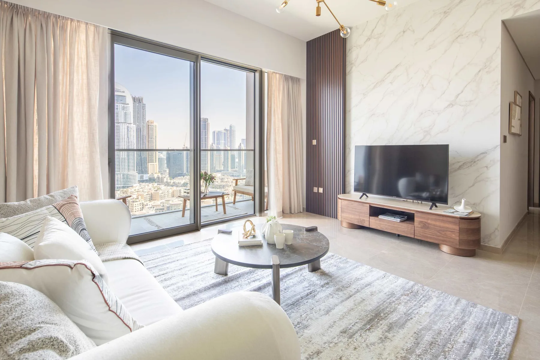 Una sala luminosa con asientos, un televisor y grandes ventanales con vistas a edificios de la ciudad.