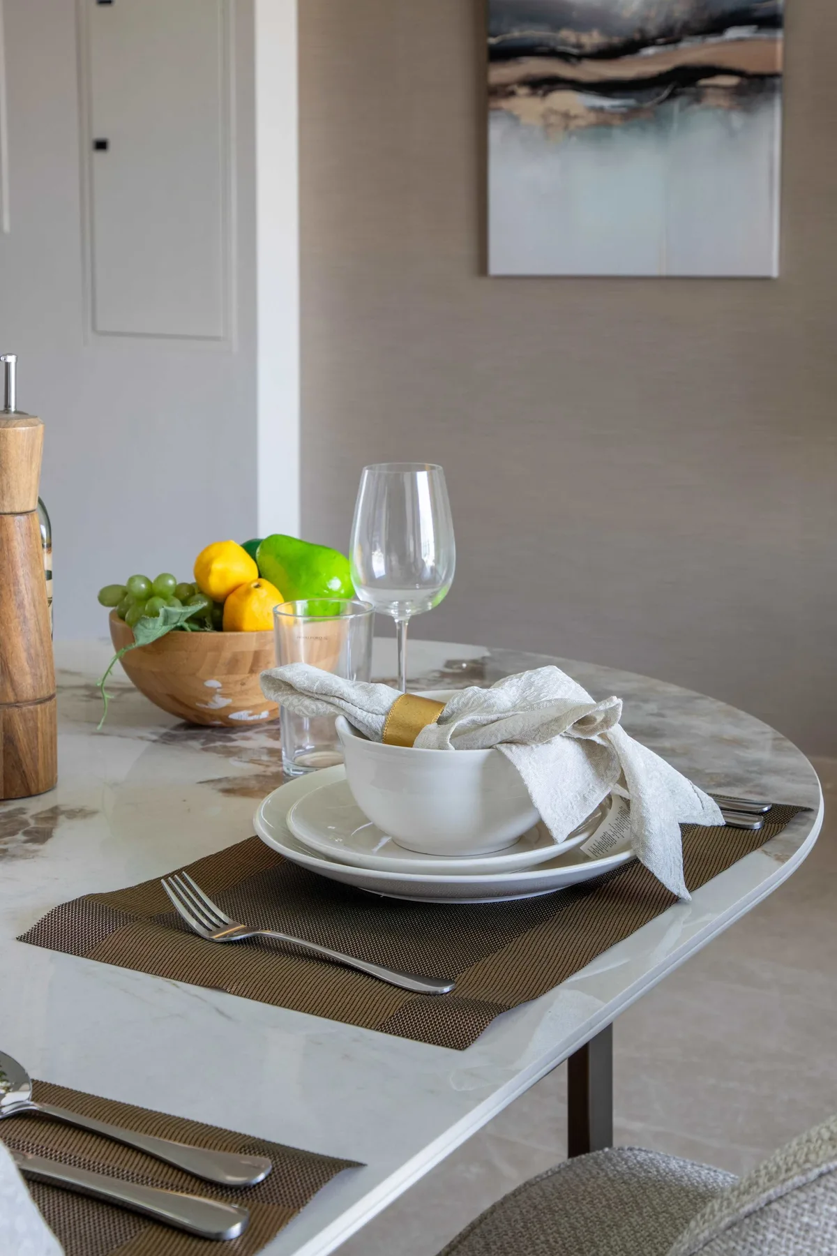 Una mesa de comedor está puesta con platos, cubiertos, fruta y una copa.