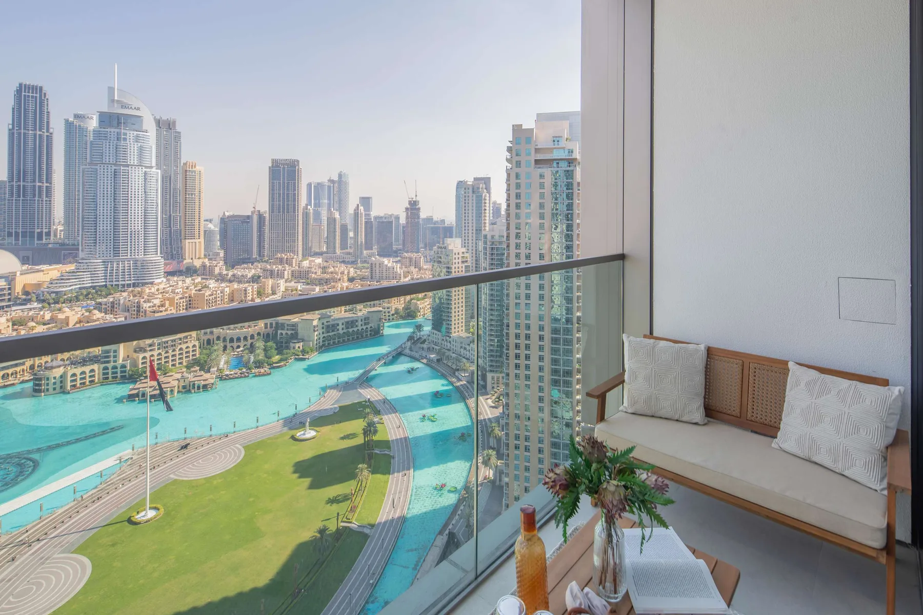 Una zona de asientos en el balcón da a una piscina turquesa, un césped verde y el perfil urbano.