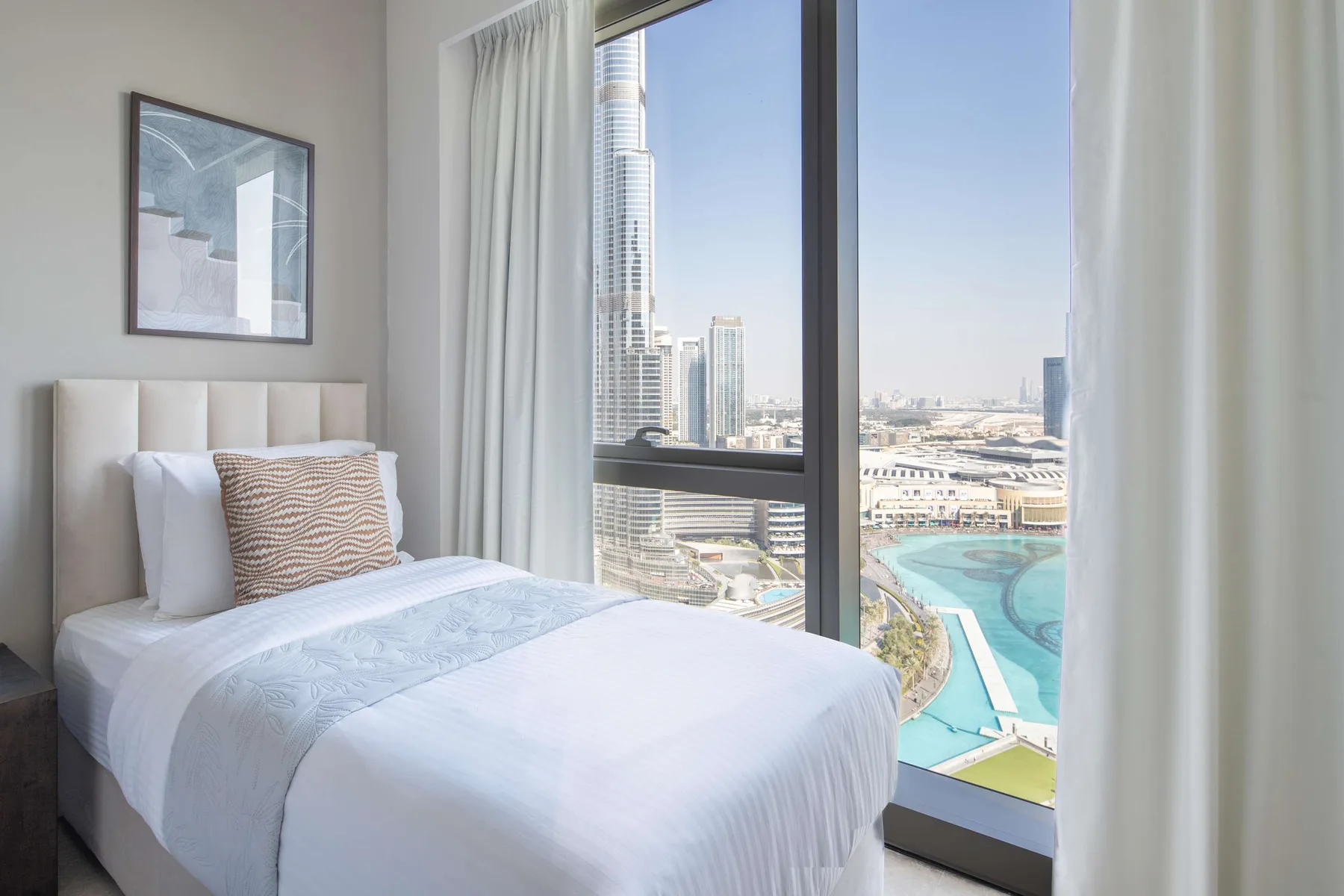 Un dormitorio con una cama bien tendida junto a una ventana amplia con vistas a la ciudad.