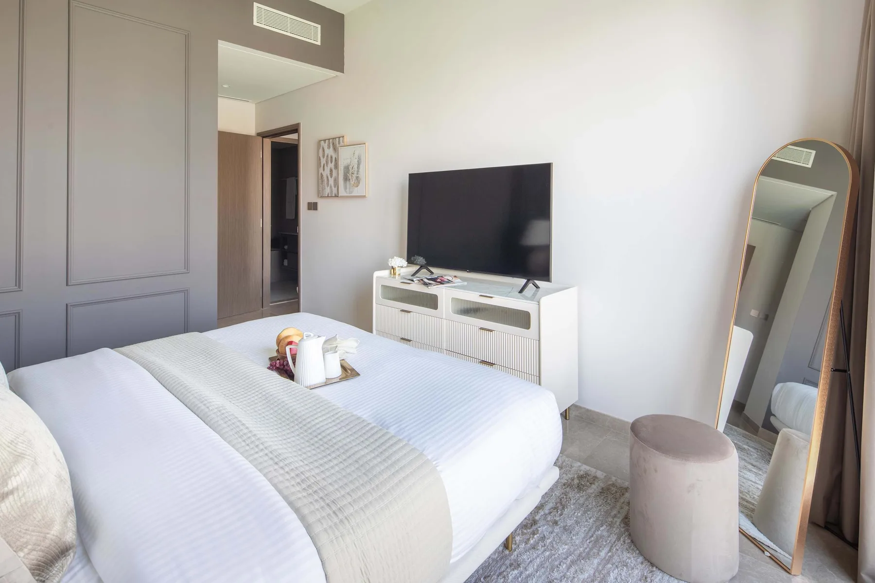 Un dormitorio luminoso con una cama tendida y un televisor sobre un mueble.