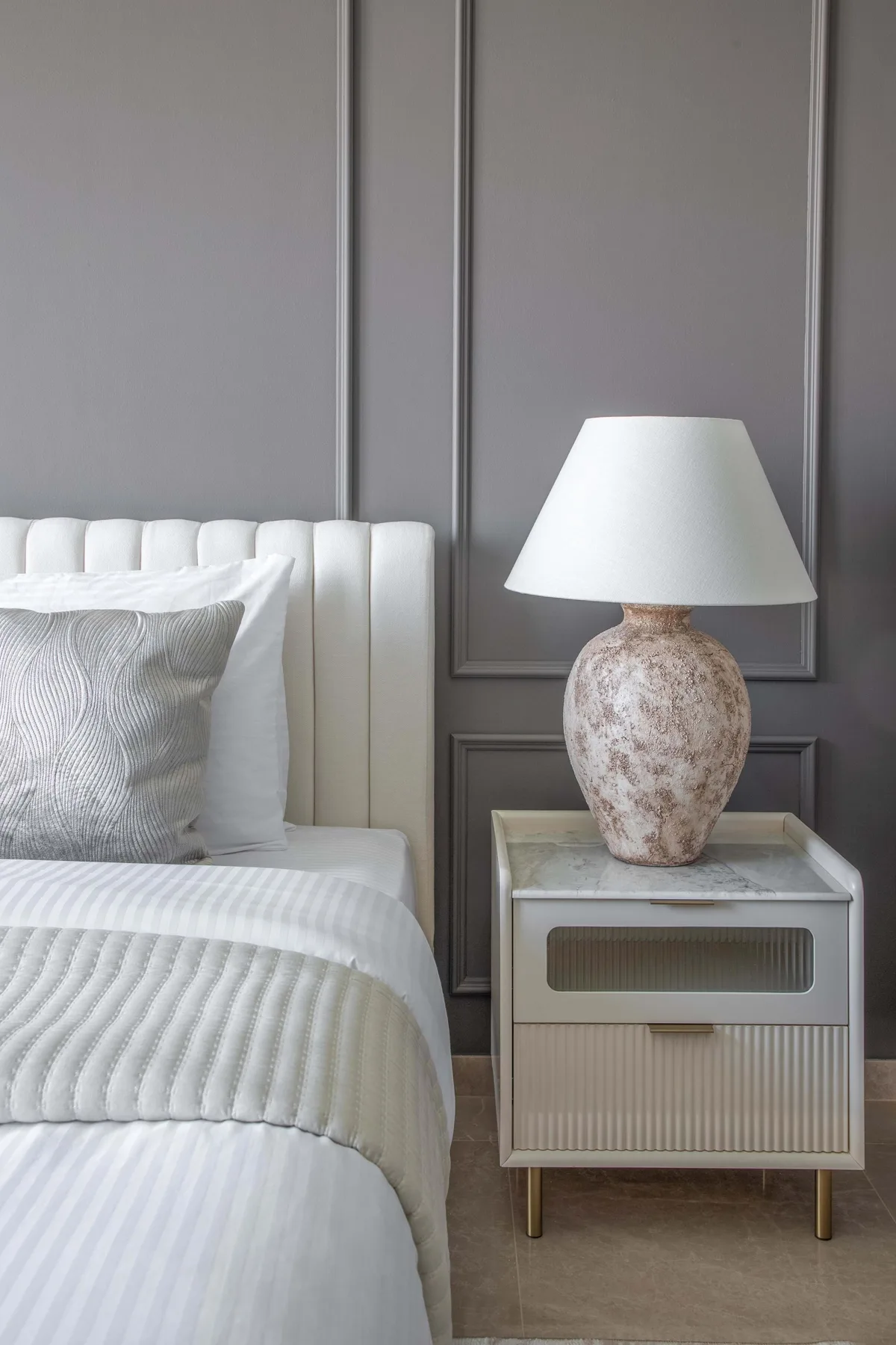 Un dormitorio con una cama blanca y una mesita de noche con una lámpara.