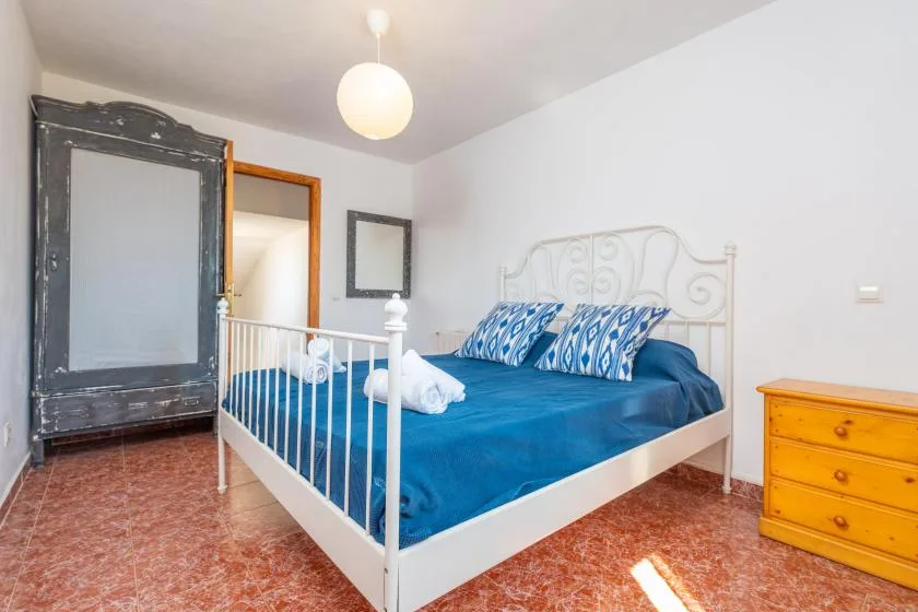 Un dormitorio con una cama blanca, ropa de cama azul y una cómoda de madera.
