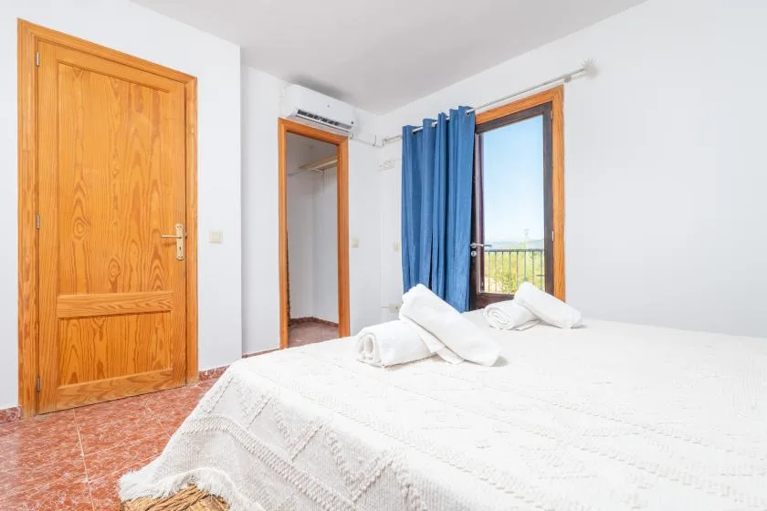 Un dormitorio luminoso con ropa de cama blanca y una cortina azul junto a la ventana.