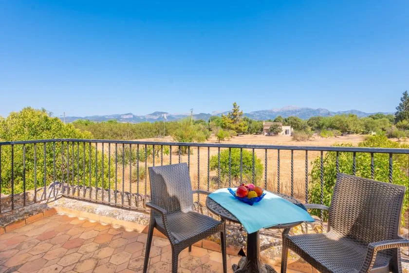 Una terraza exterior con suelo de baldosas tiene asientos junto a una mesa y da a un paisaje seco.