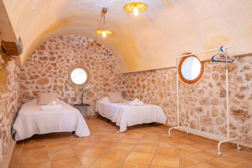 Un dormitorio con paredes de piedra, dos camas, ventanas redondas y suelo de baldosas.
