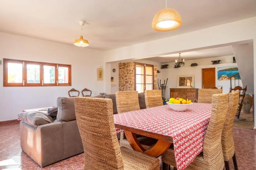 Un comedor con mantel estampado y sillas tejidas junto a una sala de estar.