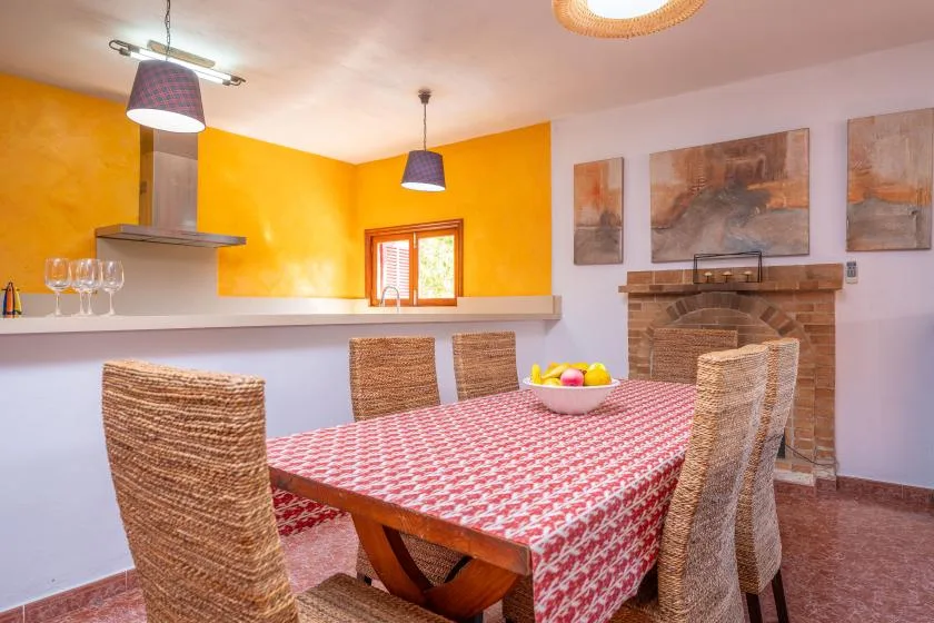 Comedor con mantel estampado, asientos tejidos y una chimenea de ladrillo.