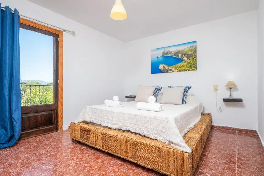 Un dormitorio con una cama, cortinas azules y una imagen costera en la pared.