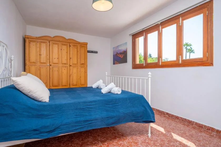 Un dormitorio con una colcha azul, un armario de madera y ventanas grandes.