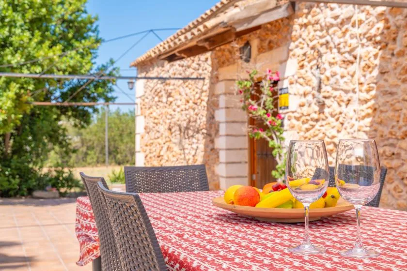 Una mesa de comedor al aire libre con fruta y copas está junto a una casa de piedra.