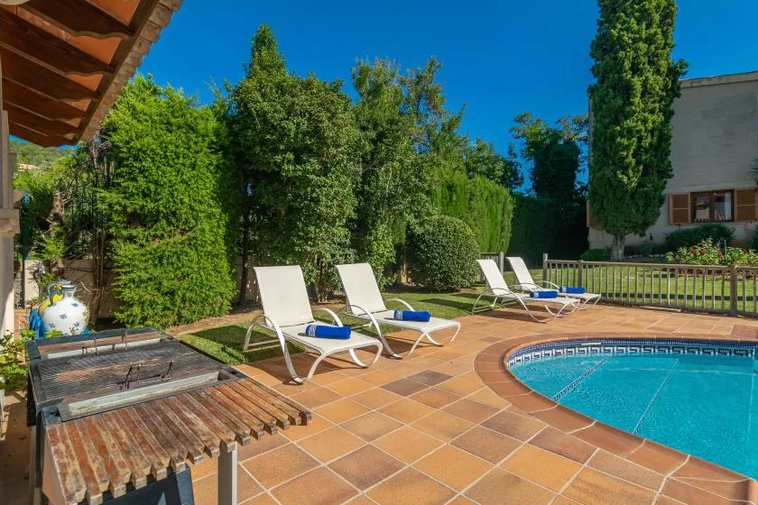 An outdoor poolside patio with lounge seating and leafy hedges.