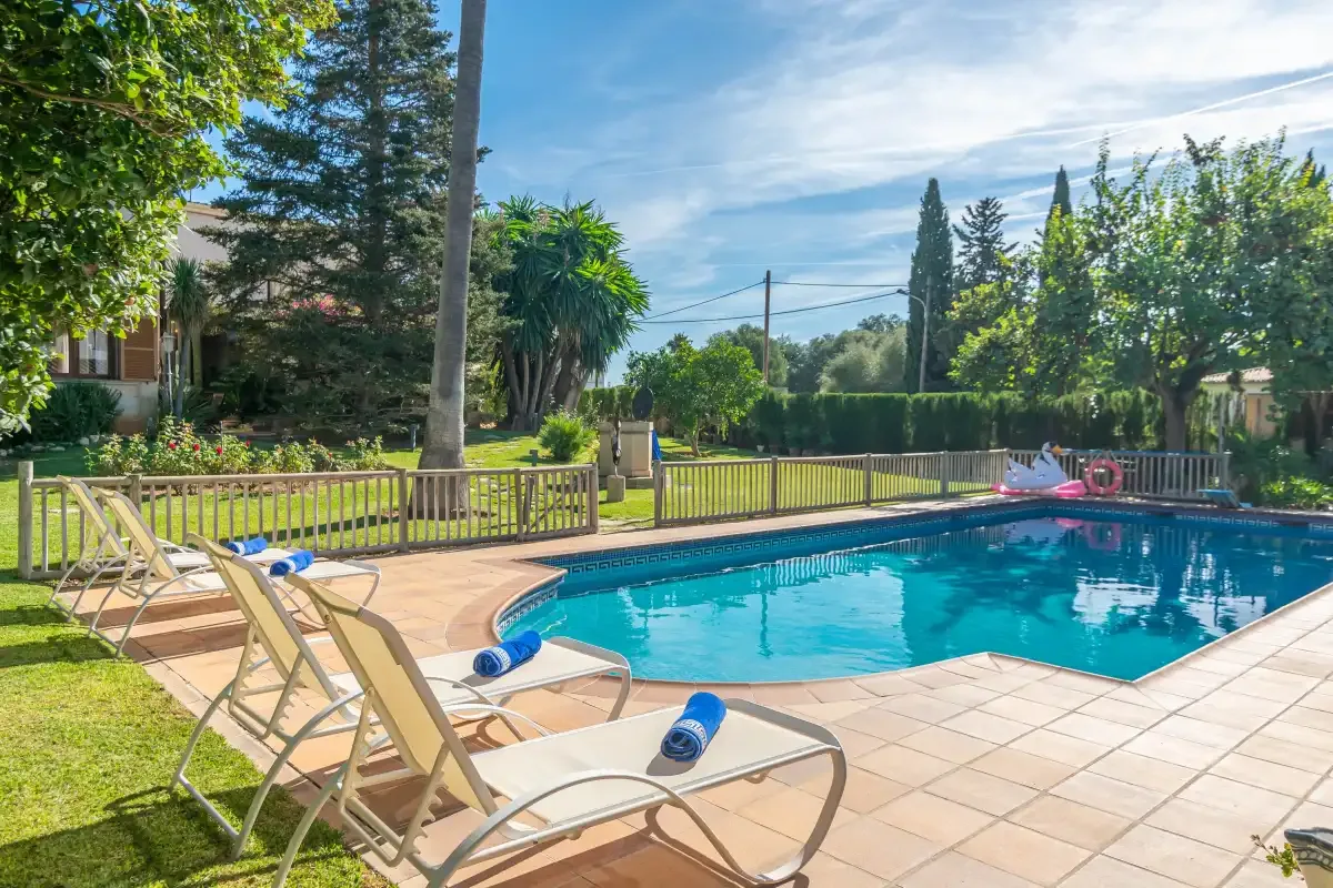 A swimming pool and lounge seating are surrounded by a sunny garden.