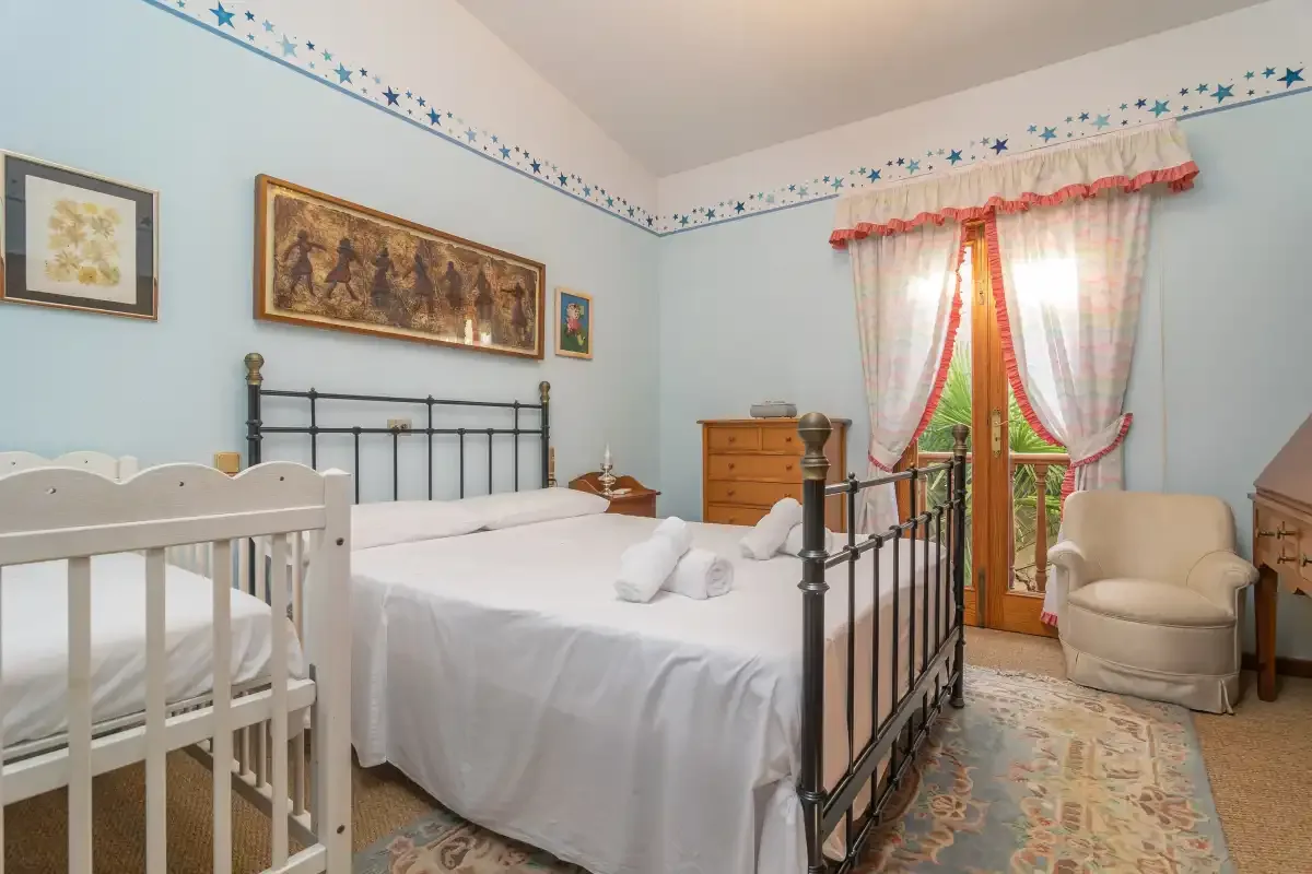 A bedroom with a large bed, a crib, and a window with curtains.