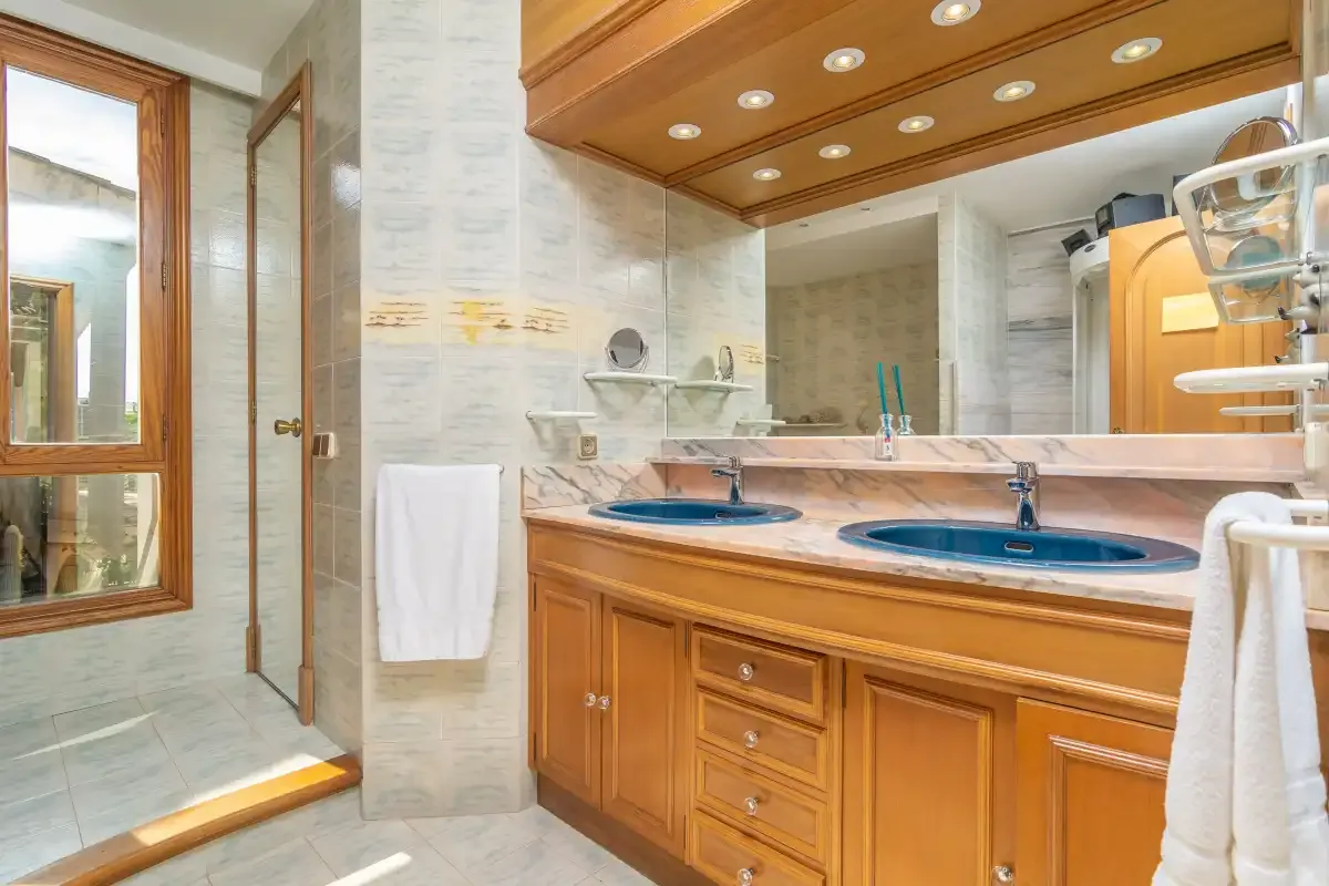 A bathroom vanity with two sinks sits beneath a wide mirror and wooden cabinetry.
