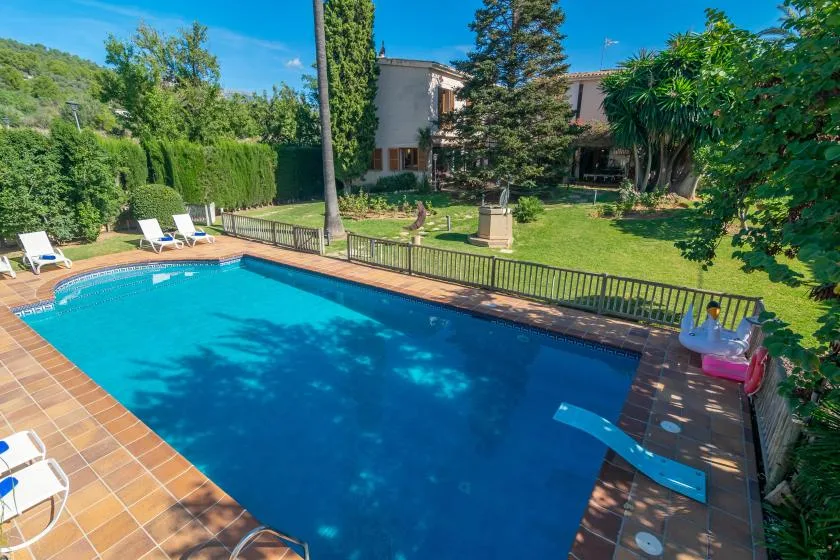 A backyard swimming pool is surrounded by tiled paving, greenery, and lounge seating.