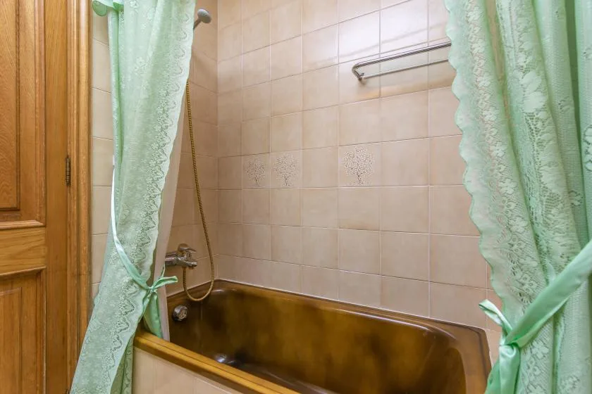 A tiled bathroom with a bathtub, shower fixture, and green curtains.