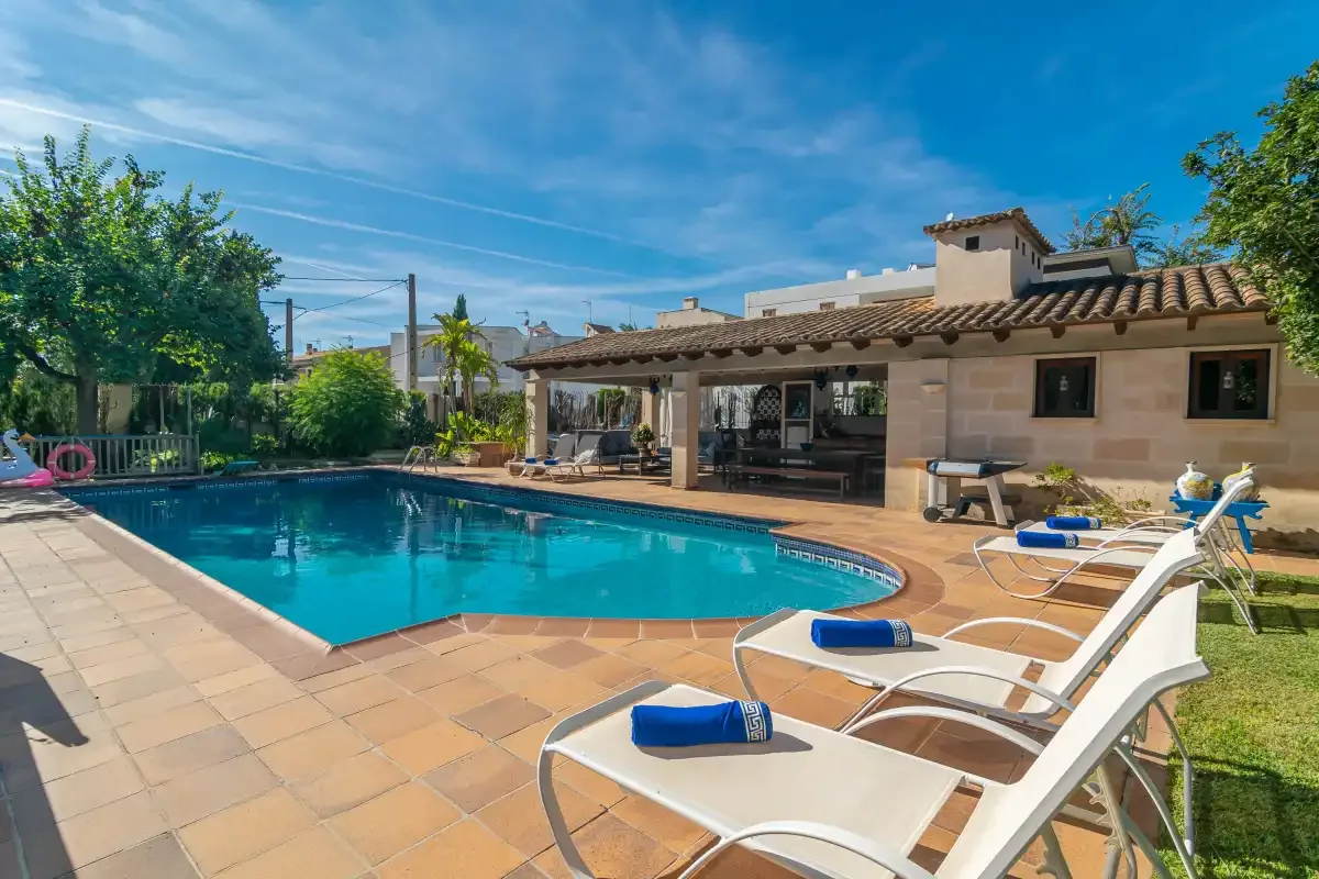 A swimming pool and sun loungers sit beside a covered patio.